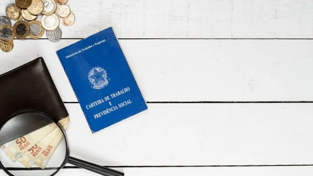 Carteira de trabalho, algumas moedas e notas de 50 reais sob uma lupa