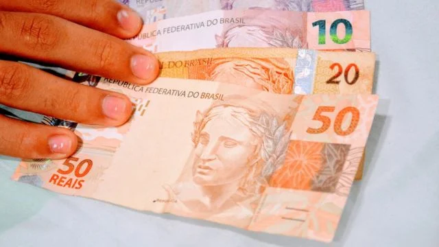 Pessoa encostando em notas de cinco, dez, vinte e cinquenta reais