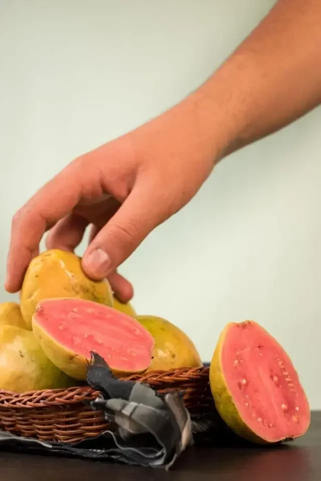 Mão pega uma goiaba de um cesto das frutas sobre uma mesa