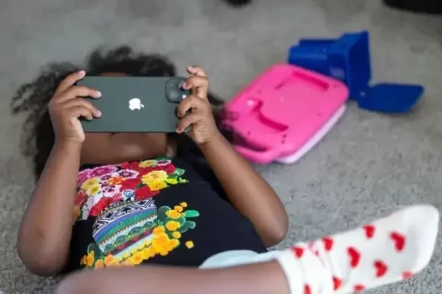 Uma criança deitada no chão e assistindo algo no celular