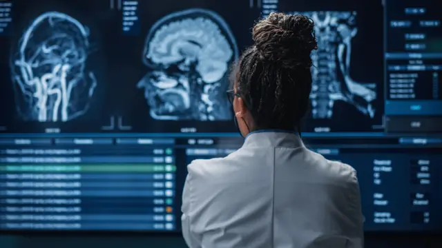 Neurologista de costas para a câmera, observando imagens do cérebro em uma tela grande à sua frente