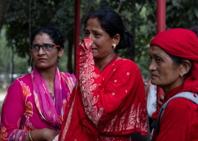 Três mulheres choram do lado de fora de um hospital após as avalanches em Trishuli Bazar