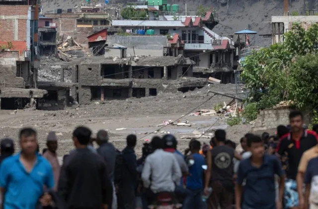 Um grupo de pessoas observa a área devastada pela enchente em Nuwakot
