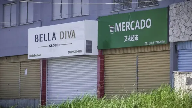 Imagem de rua comercial em Camaçari mostra loja "Bella Diva" ao lado de um mercado chinês, com ideogramas na fachada 